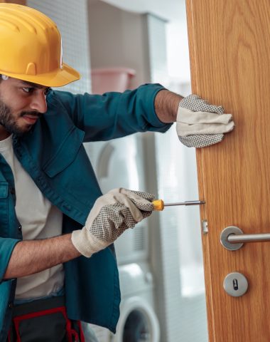 Locksmith workman in uniform installing door knob. Professional repair service